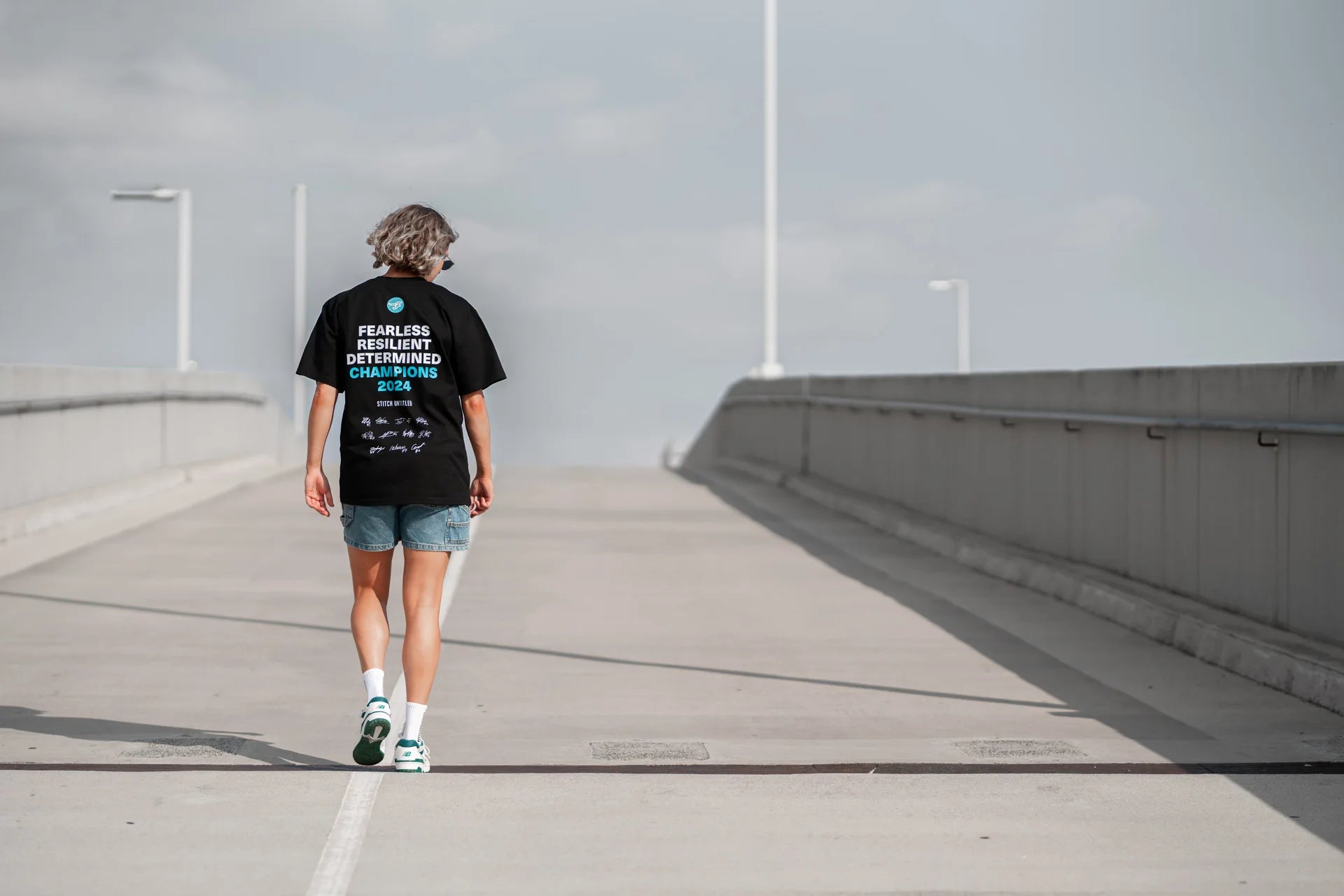 Person walking across Melbourne bridge, wearing a Stitch Untitled and Southside Flyers collaborative Champions Tee